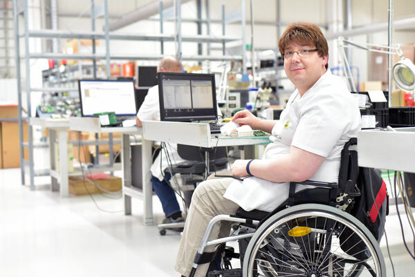 Bild vergrößern: Mann am Arbeitsplatz. Er sitzt in einem Rollstuhl.